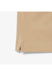 Beige kortärmad skjorta med texturerad tyg, sidsprickor i kanten och rena sömmar för en skräddarsydd look.