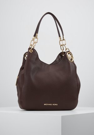Sac à main Michael Kors en cuir grainé marron foncé avec doubles anses en chaîne dorée et breloque ronde dorée avec logo, reposant sur une surface blanche.