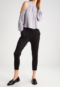 Grå kallskulder blus med plisserad front, i kombination med svarta joggerbyxor och svarta loafers. Slät tyg, lös passform och ankellängd.