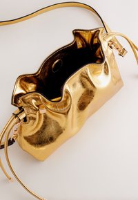 Geantă de mână metalică aurie, cu un design moale, adunat. Are interior negru, bretele reglabile și accente metalice. Deschizătura superioară facilitează accesul.