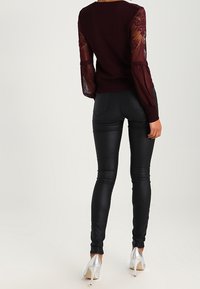 Bordeaux sweater met doorzichtige kant lange mouwen, gecombineerd met glanzende zwarte leggings en zilveren hoge hakken. Glad en aansluitend textuur.