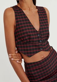 Top court à carreaux noir et rouge avec un décolleté plongeant, fermeture à boutons sur le devant, et détail froncé à la taille, fabriqué dans un tissu texturé.