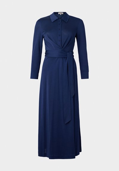 Tamsiai mėlyna suknelė su apykakle, ilgomis rankovėmis, mygtukais priekyje ir juosmens diržu. Suknelė turi apvyniojimo dizainą ir lygų paviršių. Ilgis siekia vidurinę blauzdą.