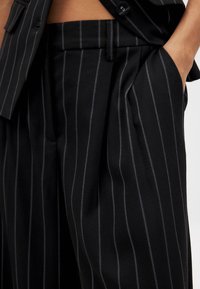 Črne hlače s črtami, izdelane iz teksturirane tkanine, z stranskimi žepi in sproščenim krojem, z gladkim pasom in subtilnim sijajem.