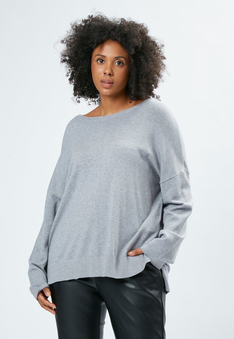 Maglione oversized grigio chiaro con scollatura ampia, polsini e orlo a coste. Textura morbida. Abbinato a pantaloni di pelle nera.