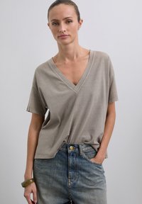 Camiseta de algodón beige con escote en V, de tejido suave y mangas cortas, combinada con jeans de mezclilla azul de cintura alta. El conjunto tiene un ajuste relajado.