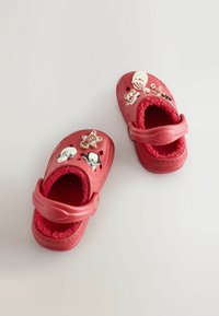 Czerwone plastikowe klapki z futrzanym wykończeniem, ozdobione naklejkami w różnych kształtach. Zamknięty przód, z regulowanym paskiem wokół kostki.