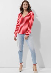 Rot-weißer gestreifter Langarmoberteil mit V-Ausschnitt und puffigen Ärmeln, kombiniert mit hellblauen Jeans, die an den Bündchen roten Akzent haben.