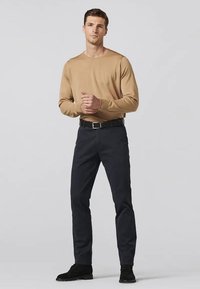 Chemise beige à manches longues, pantalon marine, chaussures noires. Design ajusté avec une texture douce et des détails de couture subtils, en pose debout sur un fond gris.