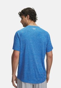 Camisa deportiva azul con un patrón texturizado en gradiente; de manga corta y cuello redondo. Logo posicionado en la parte superior de la espalda.