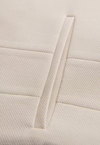 Gros plan sur un tissu beige avec des motifs rectangulaires cousus et une fente verticale ou une poche centrale.