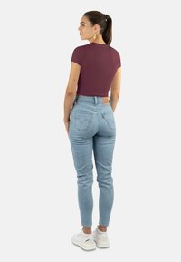Burgunderfarbenes Crop-Top mit kurzen Ärmeln, kombiniert mit hellblauen, hochgeschnittenen Jeans. Das Outfit wird mit weißen Sneakern abgerundet.