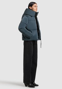 Padded teal puffer jacket with a high collar, zip closure, and side pockets. Paired with black wide-leg pants and heeled black boots.
