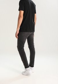 Svart t-shirt och mörkgrå jeans som bärs med vita sneakers. Kläderna har en enkel design och en avslappnad passform, som framhäver en minimalistisk stil.