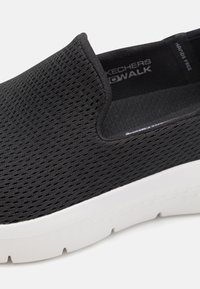 Czarne wsuwane sneakersy z przewiewną siateczką na cholewce i białą, wygodną podeszwą. Charakteryzują się gładką fakturą i brakiem widocznych zapięć.