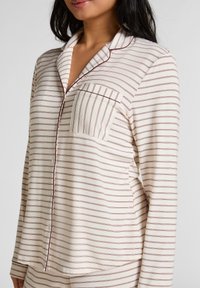 Pyjamabovenstuk met lange mouwen in crème met bordeauxrode strepen, voorzien van een kraag met inkeping, knopen aan de voorkant en één borstzak. Zachte stoftextuur.