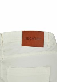 Witte stoffen broek met een bruin leren label waarop "HECHTER" staat. Bevat stikseldetails en een achterzak.