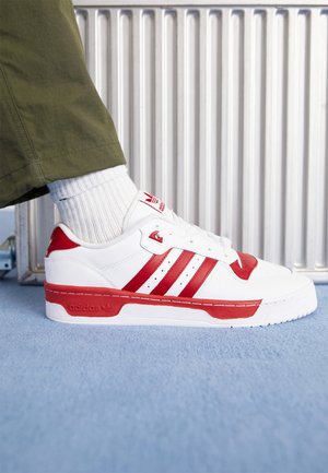 Witte sportieve schoen met rode accenten, drie rode strepen, een getextureerde neuskap en een gevoerde kraag. Heeft het adidas-logo aan de zijkant.
