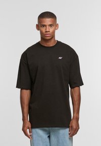 T-shirt nera in cotone con scollo rotondo e vestibilità ampia. Presenta un piccolo logo rosa sul lato sinistro del petto e maniche corte.