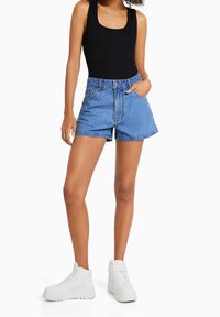 Džínové šortky ve světle modré barvě s vysokým pasem, s předními kapsami a kontrastním prošíváním, spárované s černým topem na ramínka a bílými teniskami.