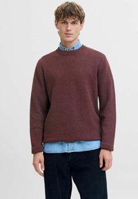Maglione bordeaux a collo rotondo con texture a coste, indossato sopra una camicia di jeans azzurri chiari, abbinato a pantaloni di velluto a coste scuri.
