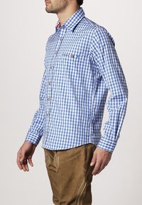 Camisa de cuadros azul y blanca con cuello abotonado, bolsillo en el pecho y botones de madera; combinada con pantalones cortos marrones.