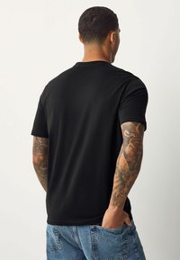 Zwarte T-shirt met korte mouwen van zacht materiaal, met een klassiek ronde hals ontwerp. De achterkant toont een gladde textuur en minimale details.
