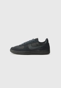 Zapatilla gris oscuro que presenta una combinación de texturas lisas y de ante, puntera redonda, cordones planos y un collar acolchado para mayor comodidad.