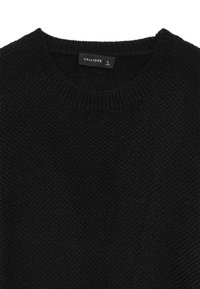 Pull en tricot noir avec un col rond et un motif texturé. L'étiquette indique la taille L. Le matériau semble doux et flexible.