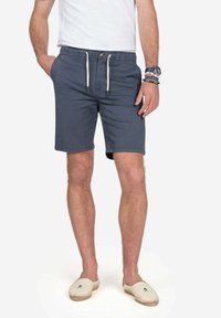 Bermudas azul marino para hombre con cintura elástica, cierre de cordón y bolsillos laterales. Combinadas con alpargatas beige y una camiseta blanca.