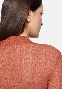 Doorzichtige kanten top in roestkleur, met een bloemenpatroon, ronde hals en een ingewikkelde textuur, die de zachte draping en delicate vormgeving benadrukt.