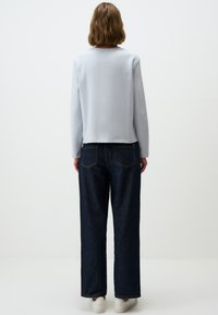 Hellblaues Sweatshirt mit langen Ärmeln und rundem Ausschnitt, kombiniert mit dunkelblauen weit geschnittenen Jeans und weißen Sneakers.