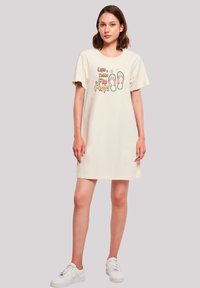 Beiges übergroßes T-Shirt-Kleid mit kurzen Ärmeln, das farbenfrohen Text "Das Leben ist besser in Flip-Flops" und Flip-Flop-Grafiken zeigt.