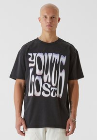 Čierne oversized bavlnené tričko s vlnkovou bielou grafickou potlačou s nápisom "ZTRATENÁ MLÁDEŽ." Okrúhly výstrih a krátke rukávy. Minimalistický dizajn.