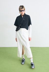 Un haut noir court avec deux poches avant, associé à une jupe blanche longueur cheville avec une fente. Des baskets grises et des lunettes de soleil complètent le look.