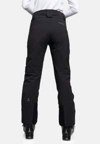 Schwarze Skihosen mit hohem Bund, Reißverschlüssen an den Knöcheln und einem eleganten Design. Mit einem Logo auf der Rückseite und maßgeschneiderter Passform für Bewegungsfreiheit.