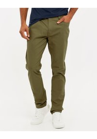 Chinos en coton vert olive avec une coupe droite, des poches latérales et une texture lisse, associés à des baskets blanches.