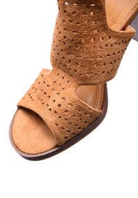 Sandal in suede marrone con upper perforato, punta aperta e suola marrone. Presenta una fascia larga e una fodera interna liscia.