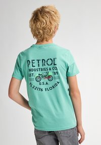 Mentolové tričko s krátkými rukávy. Na zadní straně se nachází grafika motocykly ve vintage stylu a text v námořnické modři. Vyrobeno z měkké bavlny.