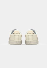 Low-top sneakers with cream leather upper, pastel accents, and textured rubber sole. Features detailed stitching and round eyelets.