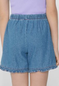 Džínové šortky s elastickým pasem, volánkovým lemem a světle modrou barvou. Mají kontrastní švy a pohodlný střih.