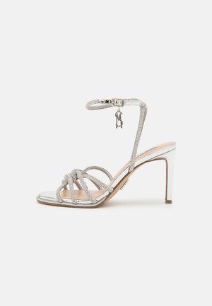 Strappy high-heeled sandal in silver with rhinestone embellishments, a metallic mirrored sole, and an adjustable ankle strap.