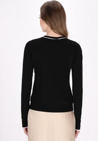 Maglione nero a maniche lunghe con collo tondo, caratterizzato da un bordo bianco sul collo. Materiale morbido, design aderente e forma semplice.