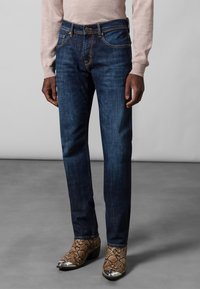 Dark blue denim jeans with a straight cut, featuring orange stitching and classic five-pocket design, paired with snake-print ankle boots.