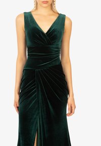 Fluwelen avonddress in diep groen, met een diepe V-hals, geplooide lijfje en zijsplit. Soepele textuur met elegante draping.