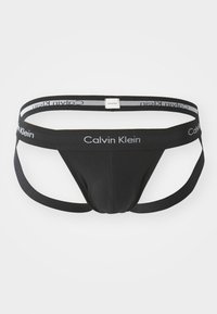 Schwarzer Calvin Klein Thong mit Stoffband, konturiertem Vorderbeutel und zwei schmalen Trägern. Verfügt über ein markiertes Logo am Bund in Grau.
