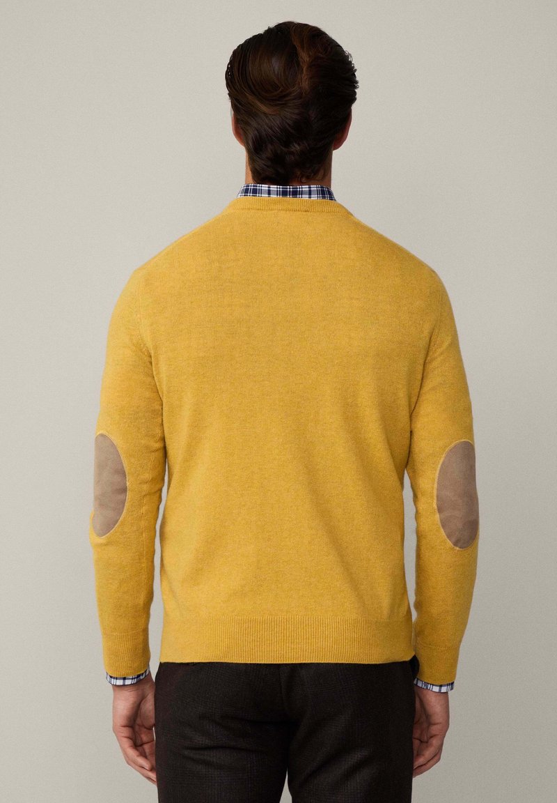 Pull jaune avec un col rond et des poignets côtelés, comportant des patchs en cuir marron aux coudes. Le matériau semble doux, avec une texture lisse.