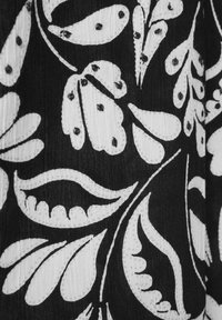 Svart tyg med ett vitt blommönster och intrikata bladdesigner, accentuerat med små svarta pärlor för ytterligare detaljer och textur.