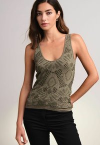 Olijf groene tanktop met een ingewikkeld kantpatroon en een ronde halslijn, gemaakt van een gestructureerd materiaal met een getailleerd silhouet. Gecombineerd met zwarte broek.
