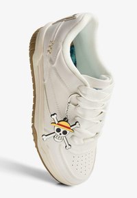 Sneaker bianca con tomaia in pelle liscia, punta tonda, perforazioni e suola in gomma. Presenta un ciondolo con teschio e ossa incrociate con un cappello di paglia.